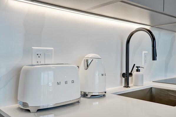 A modern kitchen with a white countertop, a toaster, a coffee maker, a sink with a faucet, and a soap dispenser.