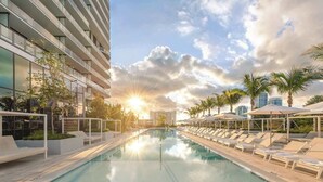 Un hôtel moderne doté d’une piscine, de chaises longues et de palmiers.