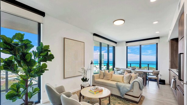 Un salon moderne avec une grande plante en pot, un canapé, une table basse et une vue sur l’océan.