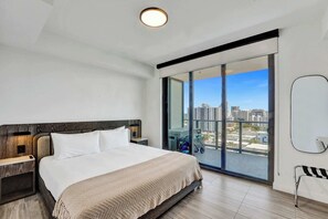 Une chambre d’hôtel moderne dotée d’un grand lit, d’une table de chevet, d’une commode, d’une grande fenêtre donnant sur la ville et d’une porte coulissante menant au balcon.
