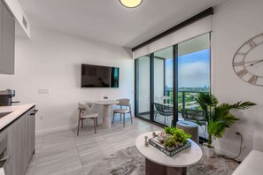A modern kitchen with a dining area, a flat-screen TV mounted on the wall, and a balcony with a city view.