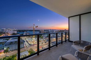 A balcony with a view of a cityscape at dusk, including a construction crane and a body of water.