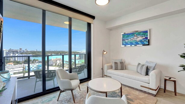 Un salon moderne avec une grande fenêtre, un canapé blanc, une table ronde et un tableau accroché au mur.