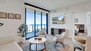 A modern living room with a large sliding glass door leading to a balcony, a round coffee table, and a flat-screen TV mounted on the wall.