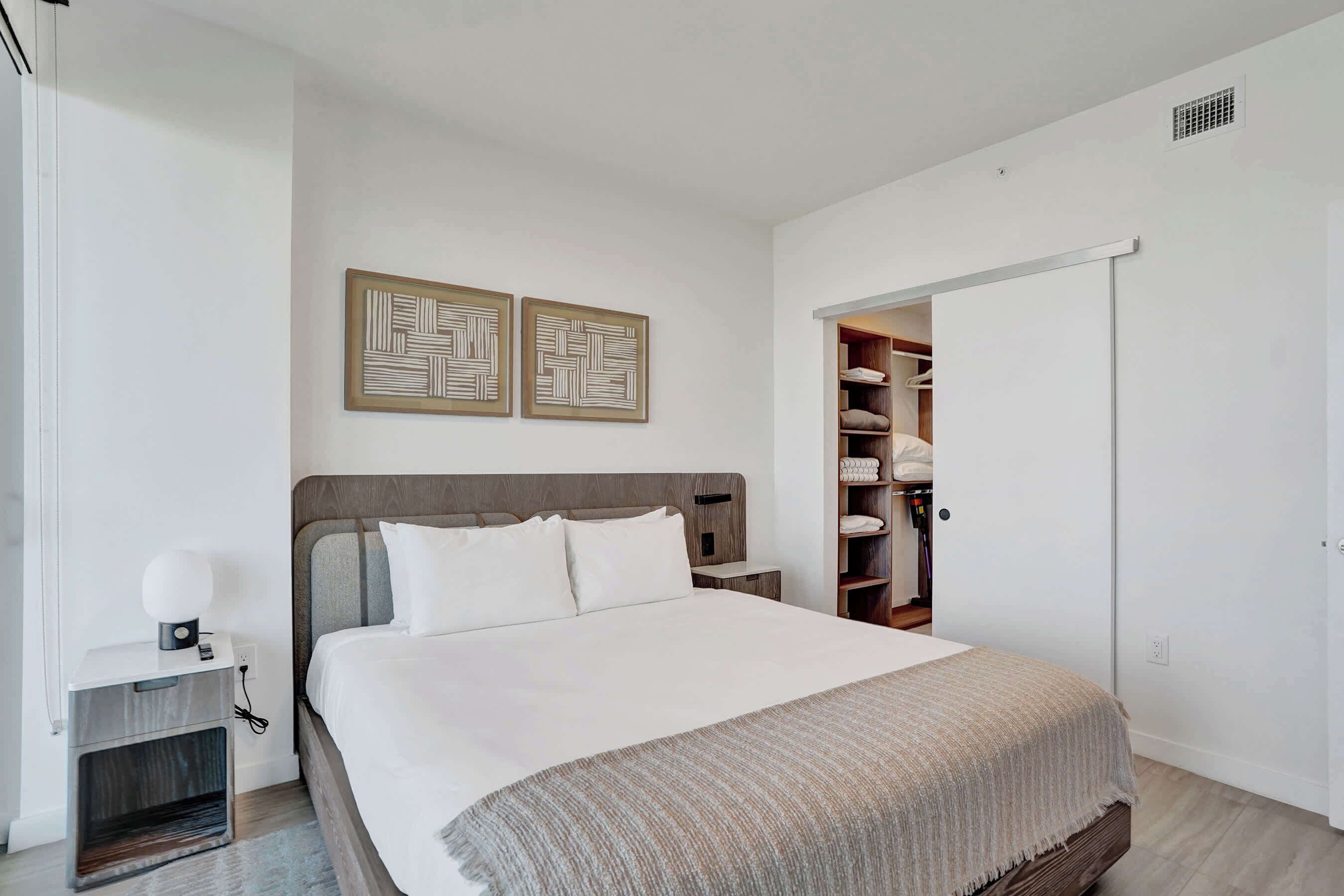 A modern bedroom with a large bed, a bedside table with a lamp, and a wardrobe.