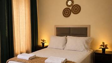A neatly made bed with a white duvet and two pillows, a bedside table with a plant, and a wall-mounted mirror.