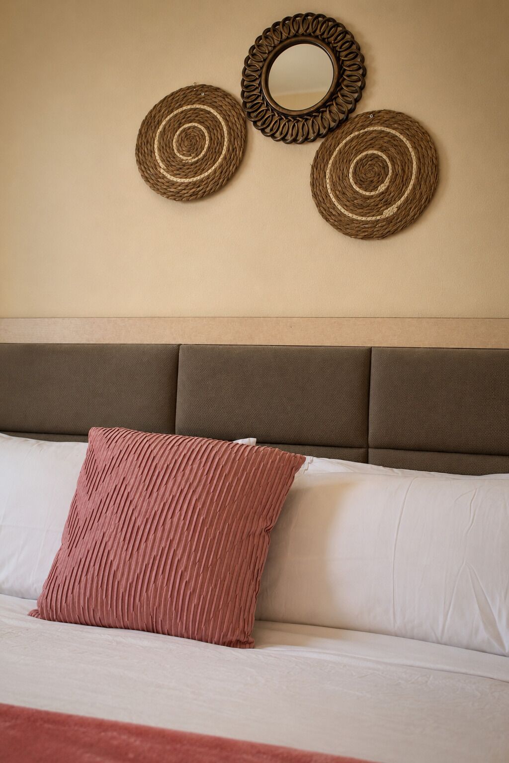 A bed with a brown headboard, a pink pillow, and three woven wall decorations.