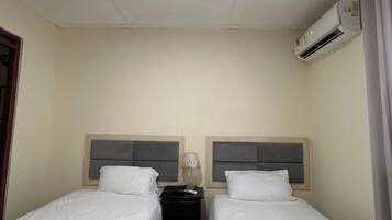 A hotel room with two single beds, a nightstand, an air conditioning unit, and a ceiling light.