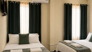 Two beds with dark green curtains, a flat-screen TV, and an air conditioning unit. - Hotel Crown Mirage (David Sur)