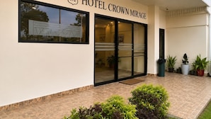 A hotel entrance with a large glass door, a sign reading 'HOTEL CROWN MIRAGE,' and potted plants in the foreground. - Hotel Crown Mirage (David Sur)