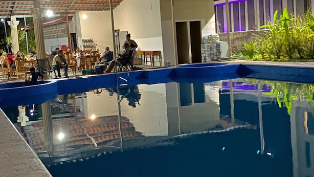 A swimming pool with a tiled deck, surrounded by a covered seating area with chairs and tables. - Hotel Crown Mirage (David Sur)