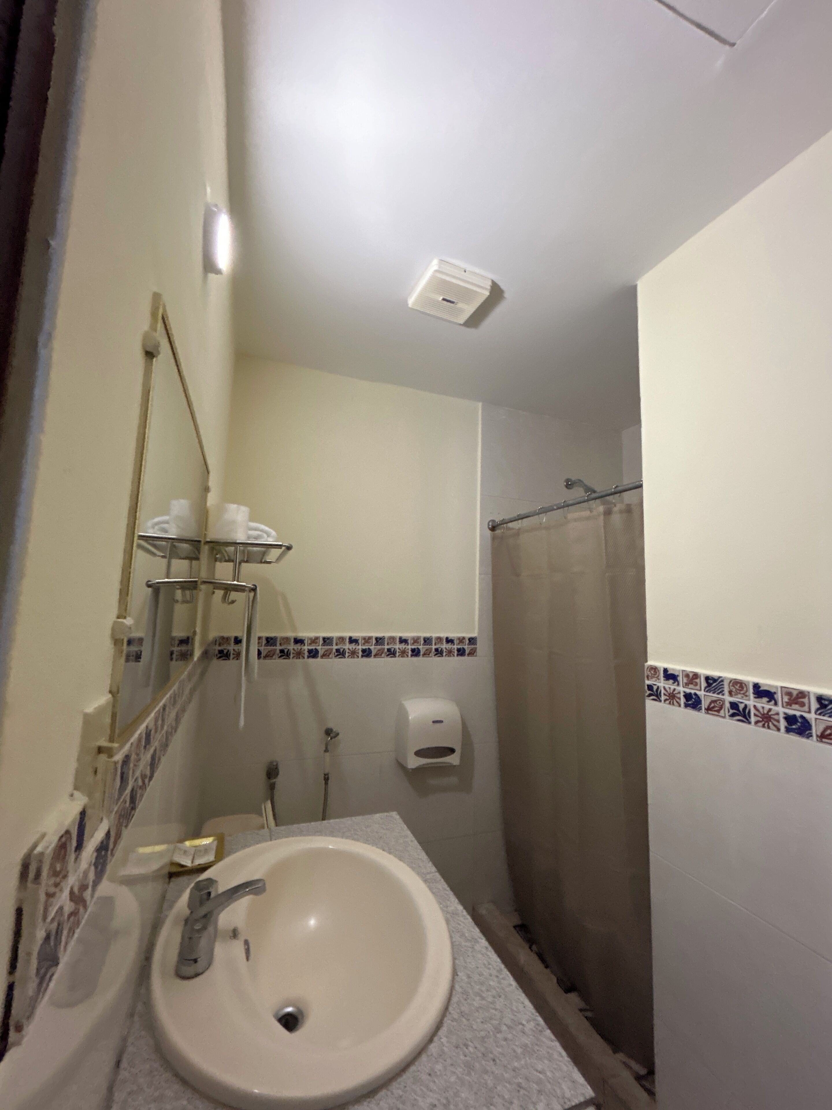 A bathroom with a sink, mirror, towel rack, shower curtain, and a hand dryer.