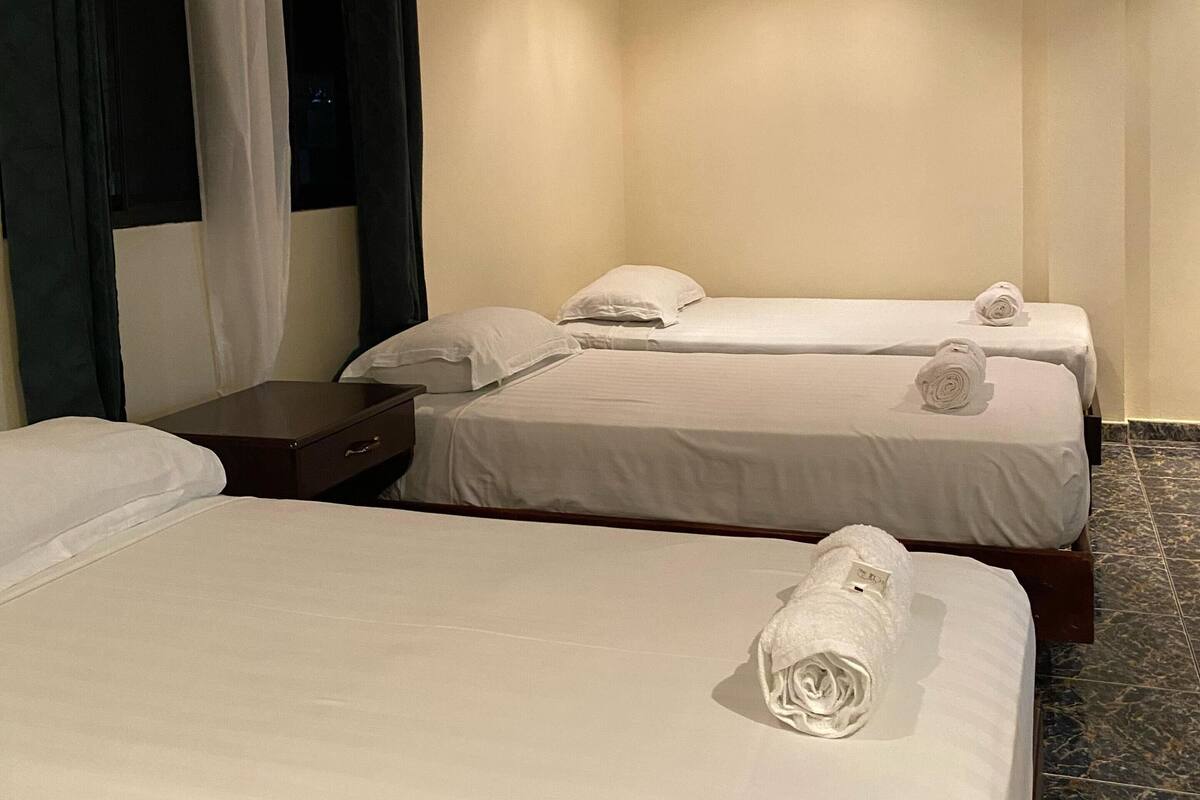 A hotel room with three beds, a chandelier, and a window with curtains.