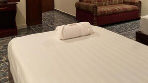 A hotel room with a bed, a red plaid sofa, a wooden door, and a mirror. - Hotel Crown Mirage (David Sur)