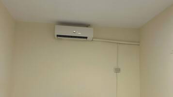 Een kleine, eenvoudige verblijfplaats met twee bedden, een nachtkastje en een airconditioning aan de muur.