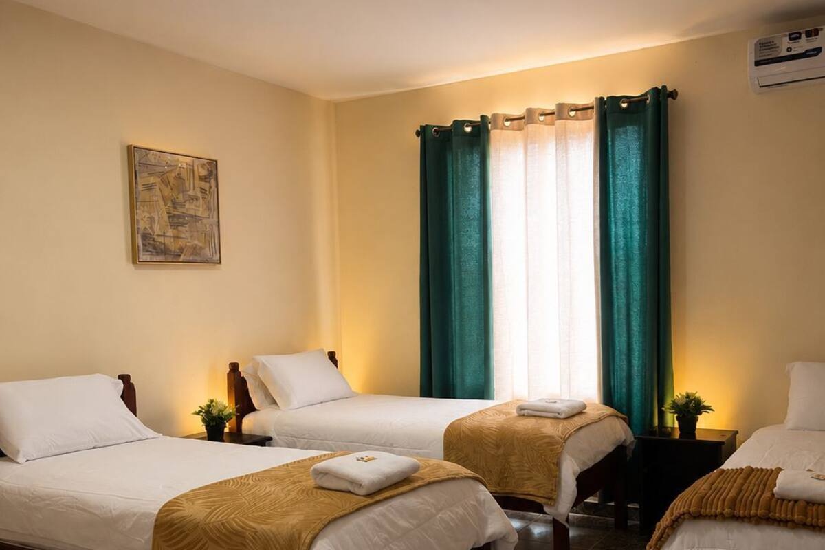 A hotel room with three beds, a painting on the wall, and a window with curtains.