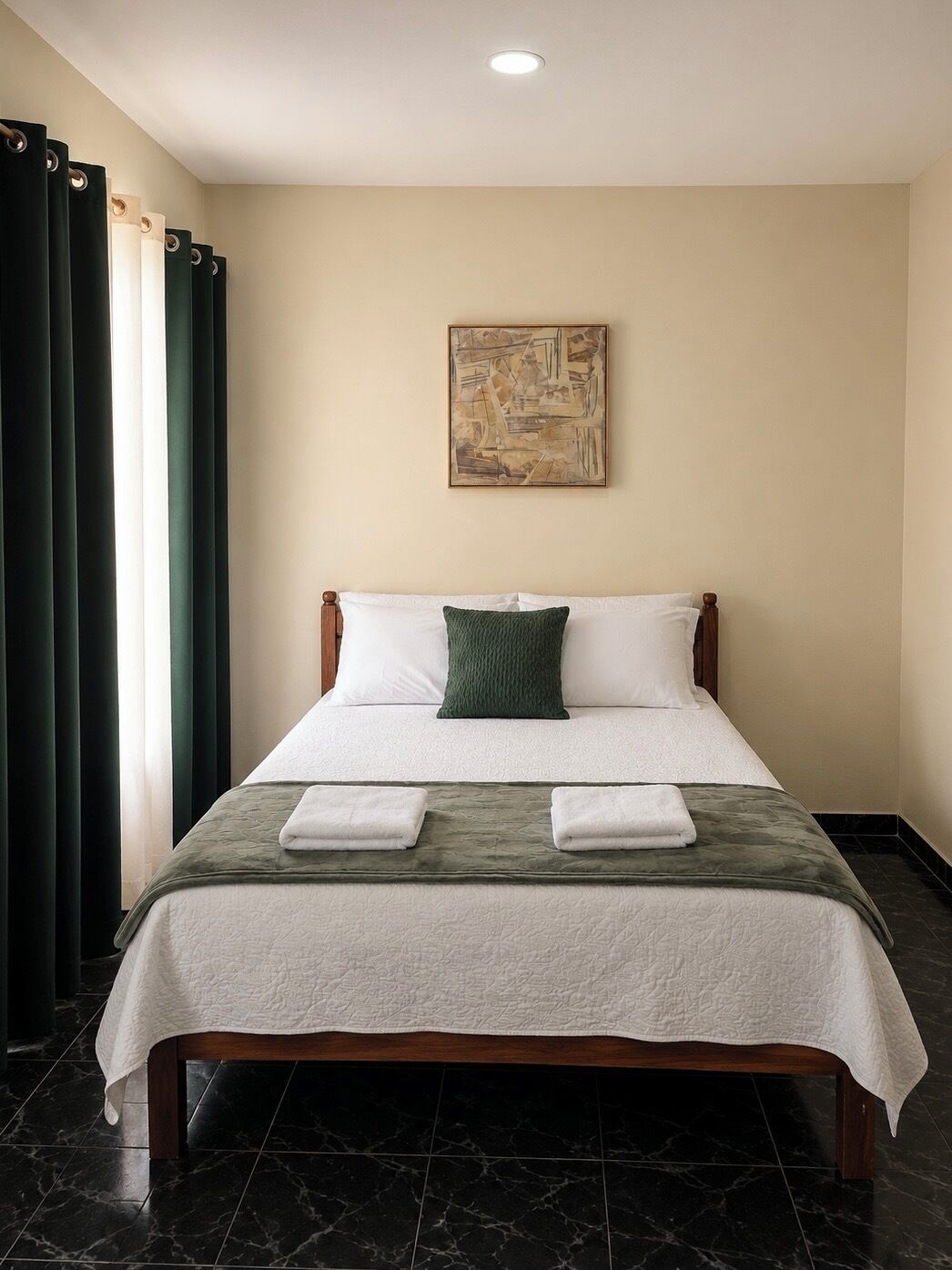 A neatly made bed with a white and green bedspread, two pillows, and two folded towels on the bed.