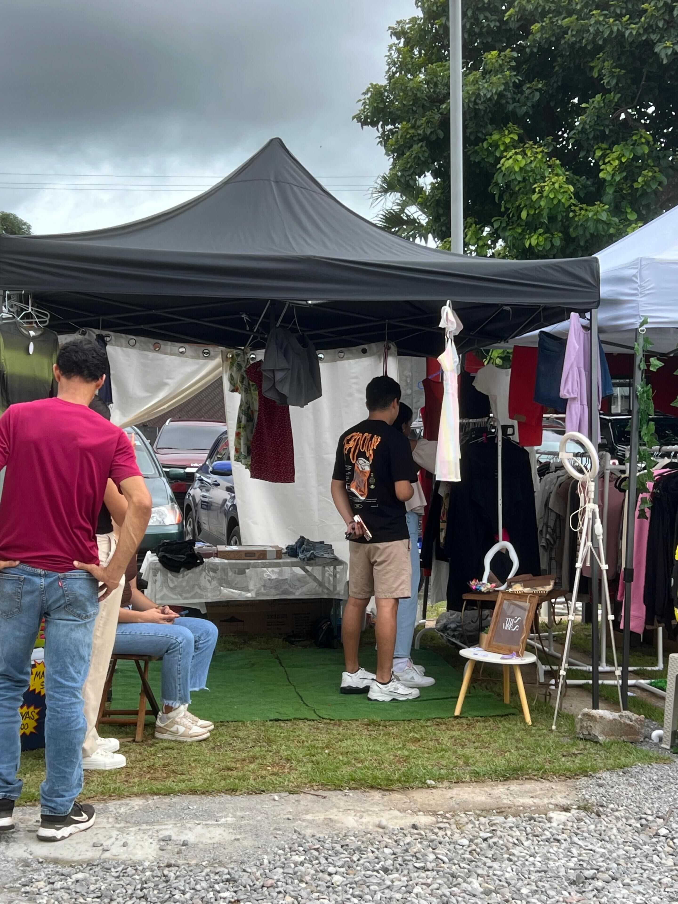 Un marché de plein air abrité sous des tentes, avec différents stands et un présentoir à vêtements.