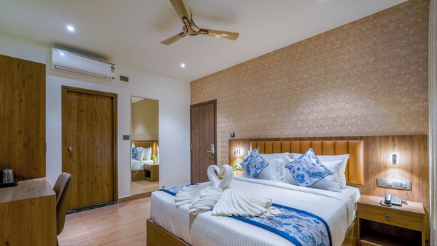 A hotel room with a large bed, wooden headboard, a desk, and a mirror. - Royal Mark (Bengaluru)