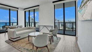 Ein modernes Wohnzimmer mit einer Couch, Sesseln, einem Couchtisch und großen Fenstern mit Blick auf die Stadt.