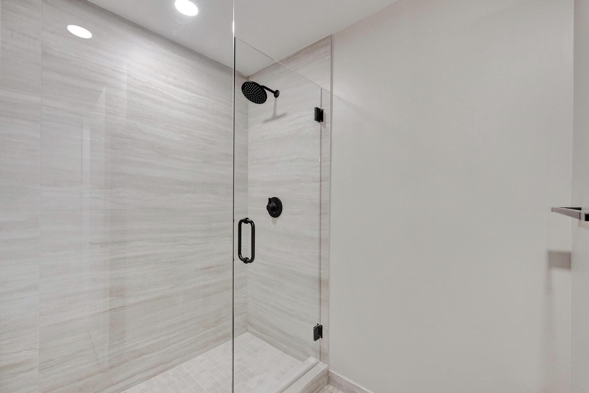 Une douche moderne dotée d’une porte en verre, d’un pommeau de douche à main et d’un panneau de commande.