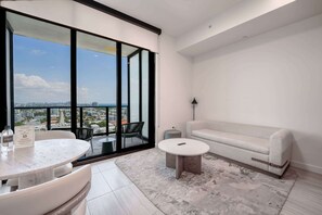 A modern living room with a large window, a round table, a sofa, and a small rug.