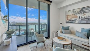 A modern living room with a large sliding glass door leading to a balcony, a sofa, a coffee table, and a painting on the wall.