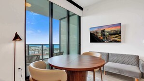 A modern living room with a round wooden table, two chairs, a grey sofa, a large window with a city view, and a framed picture on the wall. - Spacious 19th Floor 1BR Escape | Miami Beach Bliss (Miami Beach)