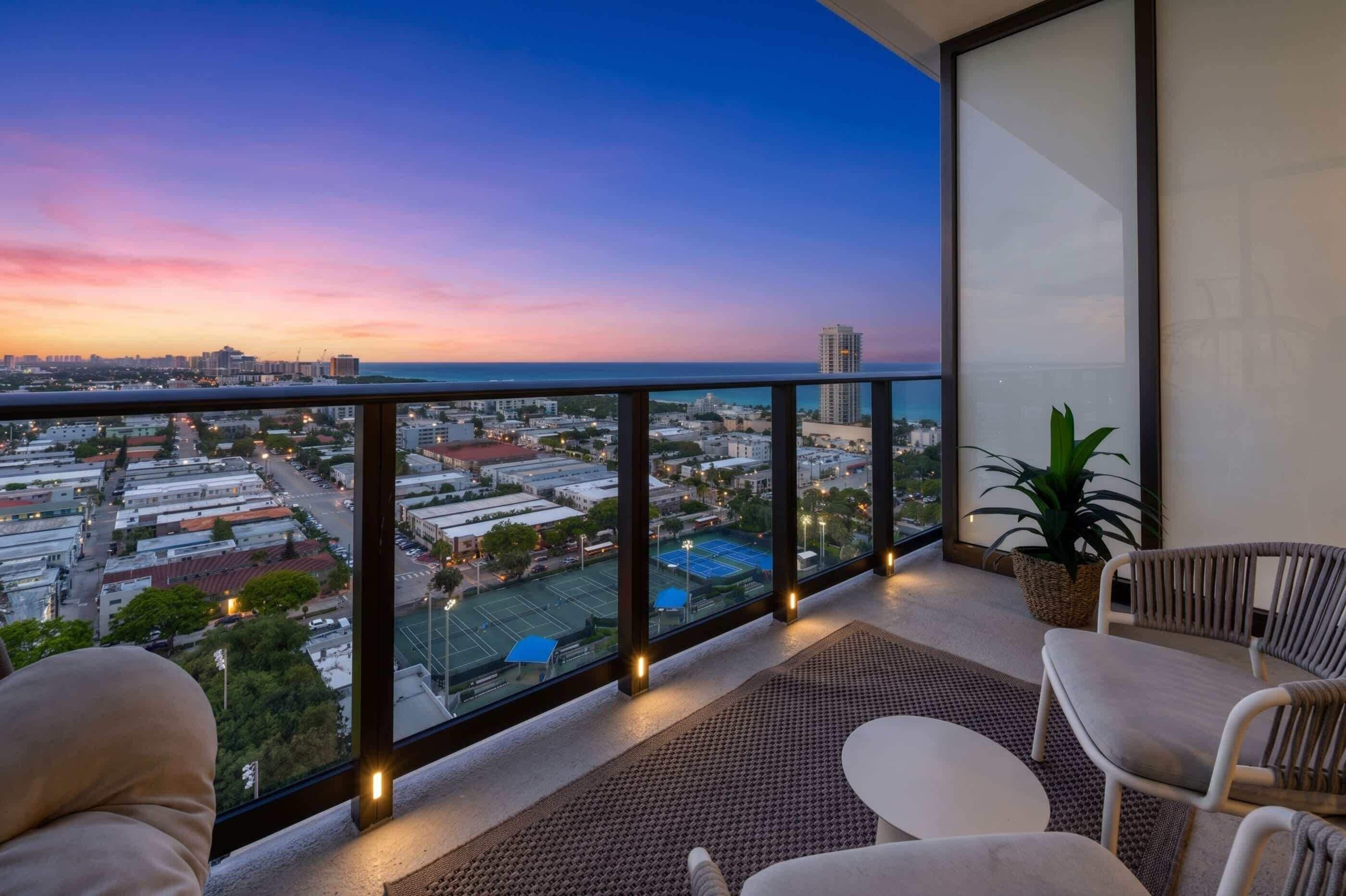 Un balcon offrant une vue sur le paysage urbain au crépuscule, avec un court de tennis et un espace détente.