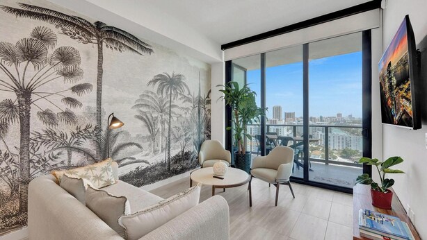 A modern living room with a large window, a sofa, a coffee table, and a potted plant. - 20th Floor Beachside Retreat | Pool & Ocean Views (Miami Beach)