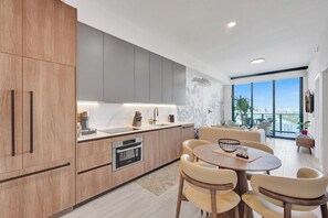 Une cuisine moderne dotée d’un four encastré, un coin repas avec une table ronde et des chaises, et une grande fenêtre offrant une vue sur la ville.