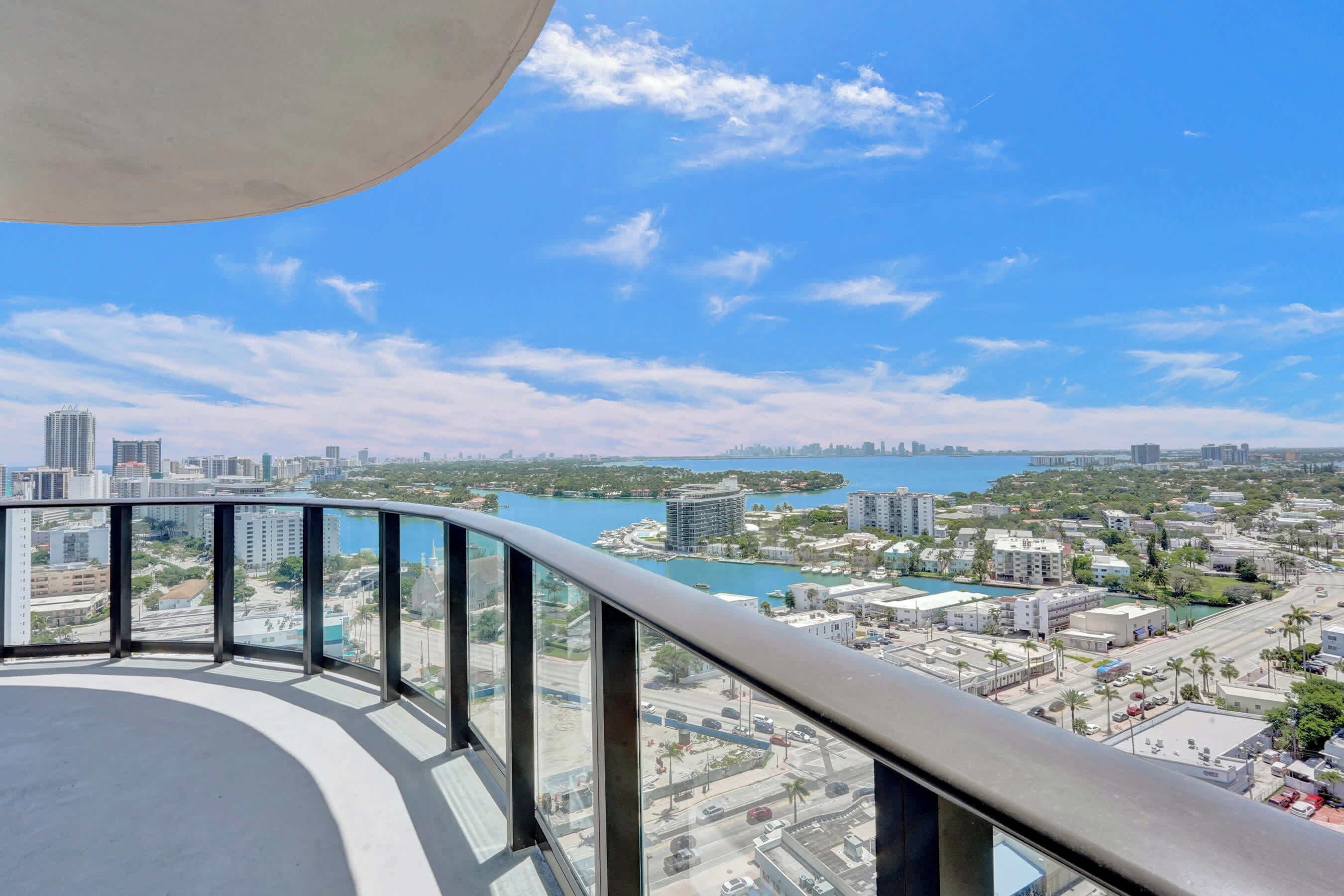 A high-rise building with a view of a cityscape, including a body of water and greenery.