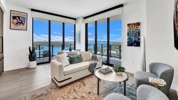 A modern living room with a sofa, armchairs, a coffee table, and a large window with a city view. - 20th Floor Luxe Escape | Pool, Gym & Beach Access (Miami Beach)