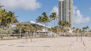 A beach with a high-rise hotel, palm trees, and a volleyball net. - 20th Floor Urban Coastal Escape | Oceanview 1BR (Miami Beach)