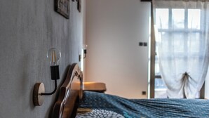 Une chambre à coucher avec une tête de lit en bois, un luminaire fixé au mur et une fenêtre ornée de rideaux légers.
