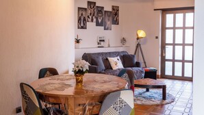 Un salon chaleureux avec une table ronde en bois, un canapé et une table basse. On y trouve également des œuvres d’art murales, une lampe et une porte avec une fenêtre.