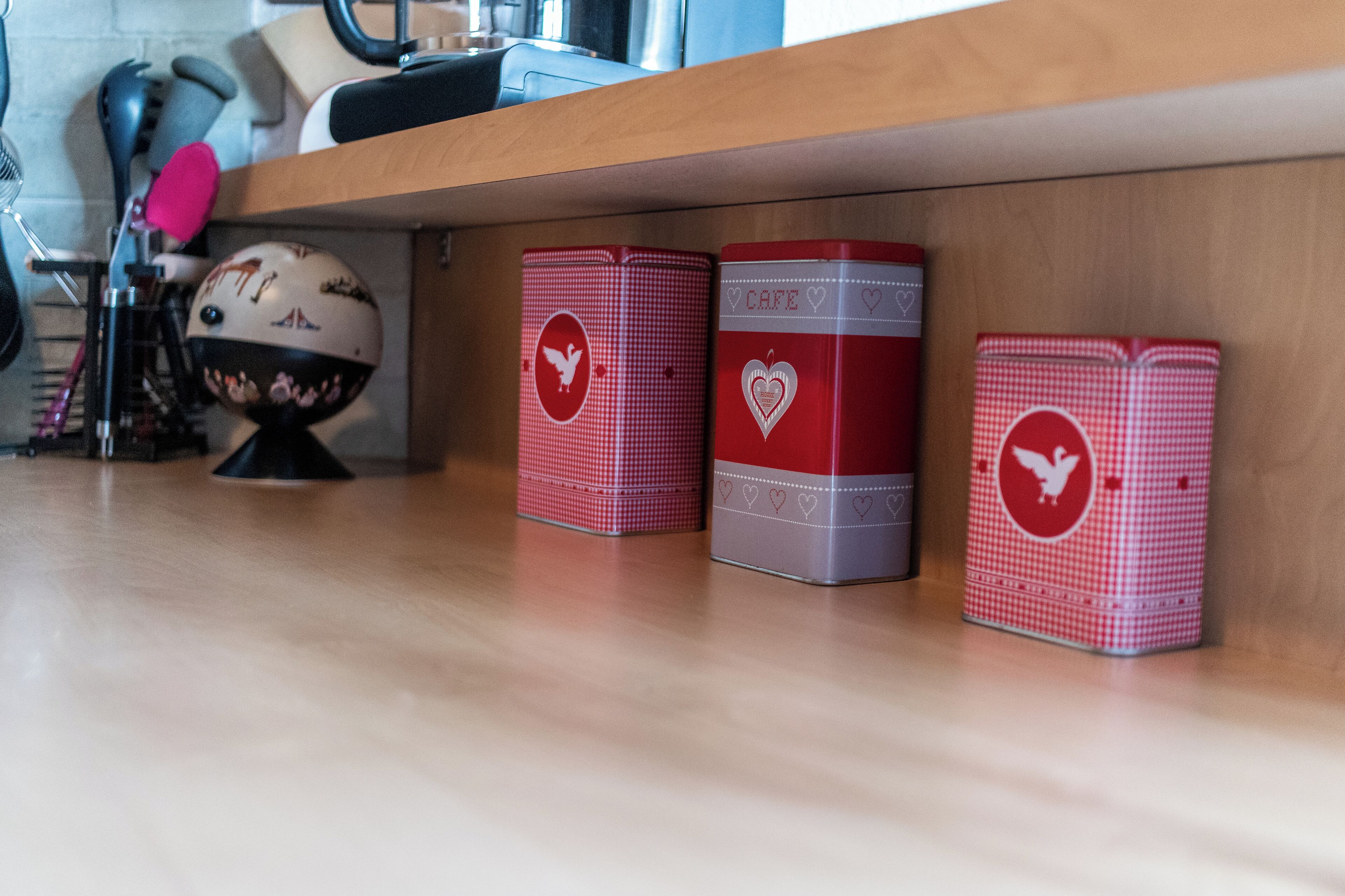 Tres cajas de almacenamiento rojas y plateadas con diseños de corazón y paloma sobre un estante de madera.