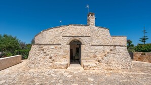 A stone building with an arched entrance, a chimney, and a flag on top. - Trullo Giuseppe by Rentbeat (Ostuni)