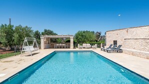 A rectangular swimming pool with a pergola and lounge chairs on one side, and a stone building on the other. - Trullo Giuseppe by Rentbeat (Ostuni)