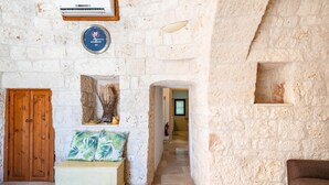A stone-walled room with a wooden door, a white cabinet, and a bed with green pillows. - Trullo Giuseppe by Rentbeat (Ostuni)