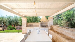 An outdoor kitchen with a stone wall, a table, and chairs. - Trullo Giuseppe by Rentbeat (Ostuni)