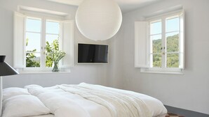 Une chambre à coucher comprenant un lit, deux fenêtres, un téléviseur à écran plat et un luminaire suspendu.