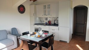 Uma cozinha compacta com armários brancos, uma mesa de jantar com cadeiras e um relógio na parede.