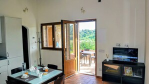 Cozinha moderna com área de refeições, TV e varanda com vista para o verde.