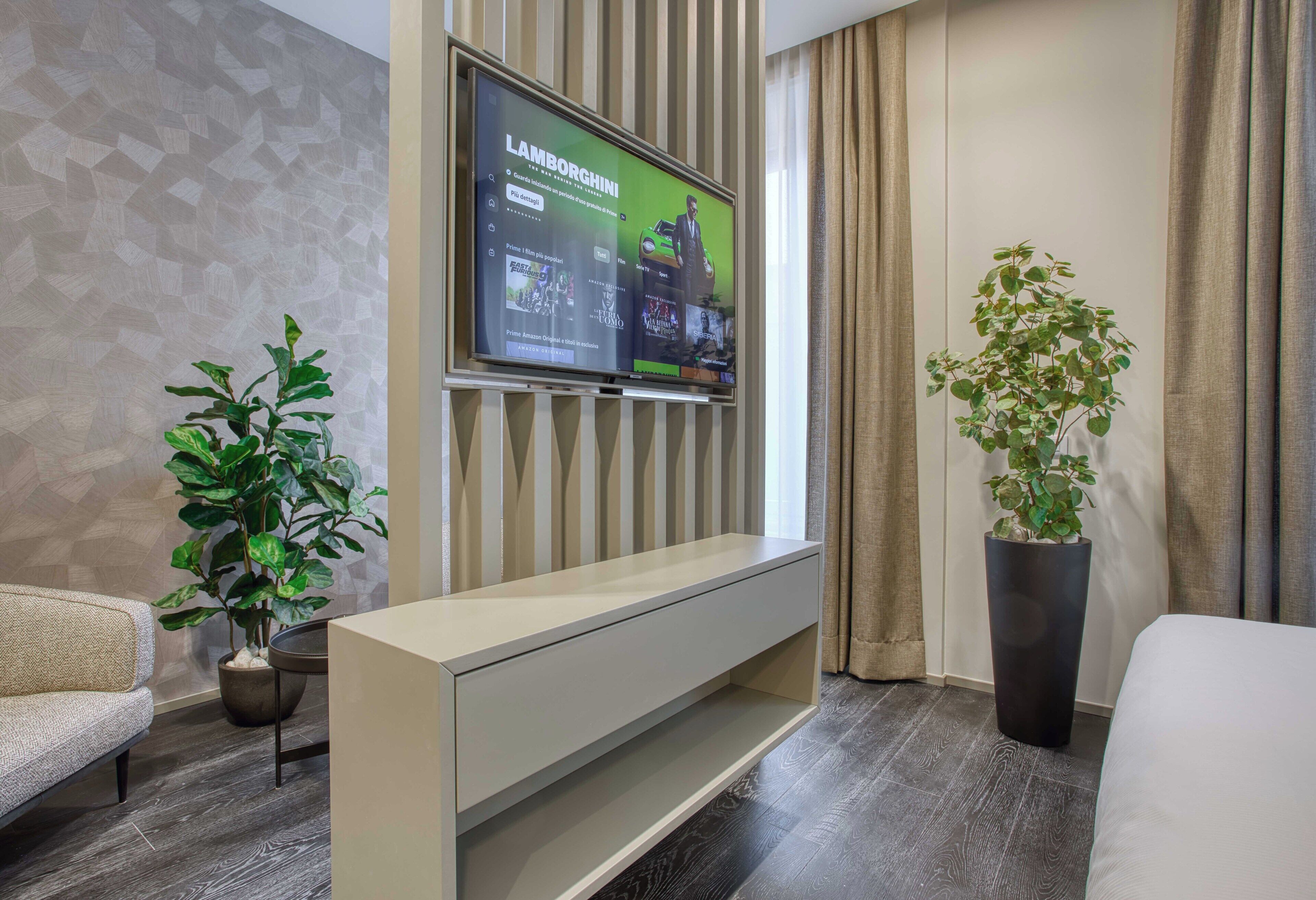 Un salon moderne avec un téléviseur à écran plat fixé au mur, un canapé, une table basse et deux plantes en pot.
