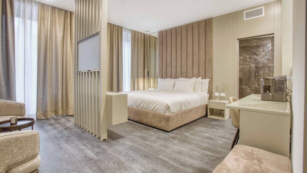 A modern hotel room with a large bed, a desk, a chair, and a television.