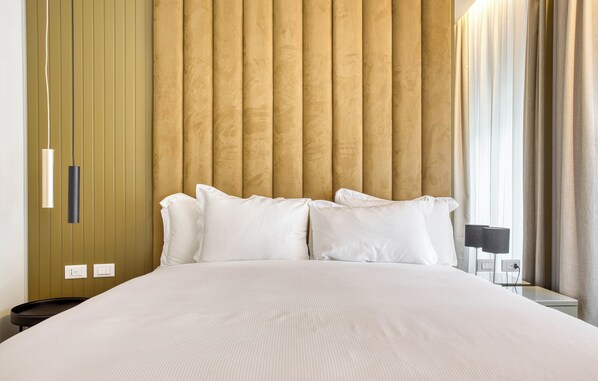 Habitación de hotel con una cama grande, cabecera de madera, mesita de noche con lámpara y ventana con cortinas.