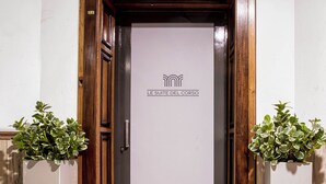 A hotel entrance with a wooden door, a tiled floor, and two potted plants.