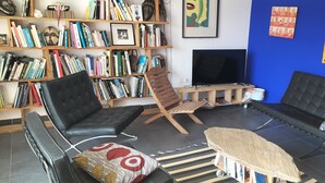 A modern living room with a black leather sofa, a wooden chair, and a bookshelf filled with books.