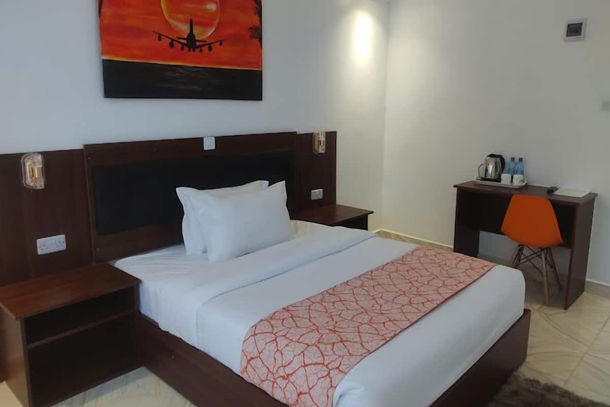 A hotel room with a bed, a desk, and a chair. There is a painting on the wall above the bed.